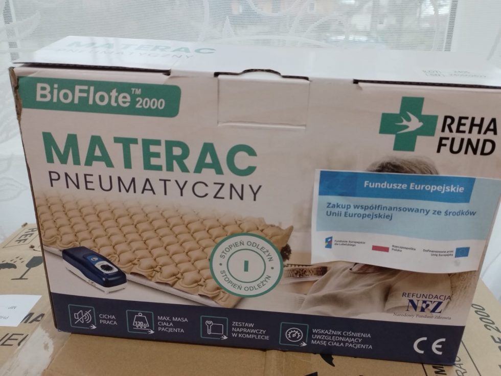 Opakowanie pneumatycznego materaca marki BioFlote 2000 firmy Reha Fund. Na froncie widoczne jest zdjęcie materaca z kontrolerem, logo producenta oraz napis „MATERAC PNEUMATYCZNY”. Umieszczono również oznaczenie „Fundusze Europejskie” i informację o współfinansowaniu zakupu ze środków Unii Europejskiej. Na dolnej części opakowania znajdują się ikony i opisy dotyczące cichej pracy urządzenia, maksymalnej masy pacjenta, zestawu naprawczego w komplecie oraz wskaźnika ciśnienia uwzględniającego masę ciała pacjenta.