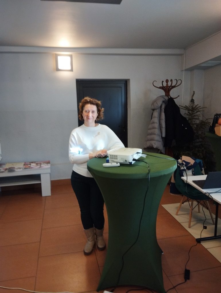 Zdjęcie przedstawia pomieszczenie oraz kobietę stojącą za zielonym stojakiem, na którym znajduje się projektor.