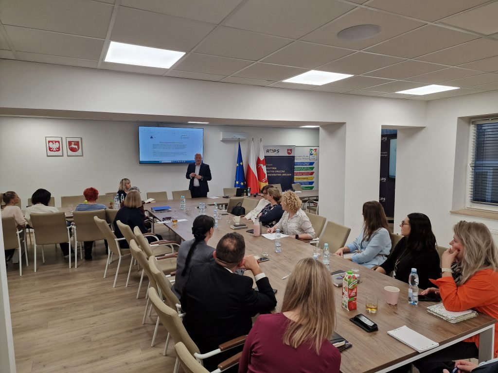 Uczestnicy szkolenia siedzą przy stołach i słuchają prowadzącego szkolenie.