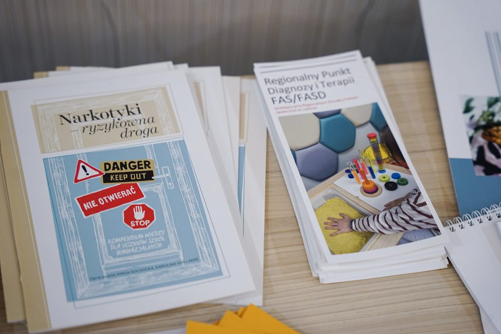 Na stole leżą broszury i materiały drukowane. Widoczne okładki publikacji.