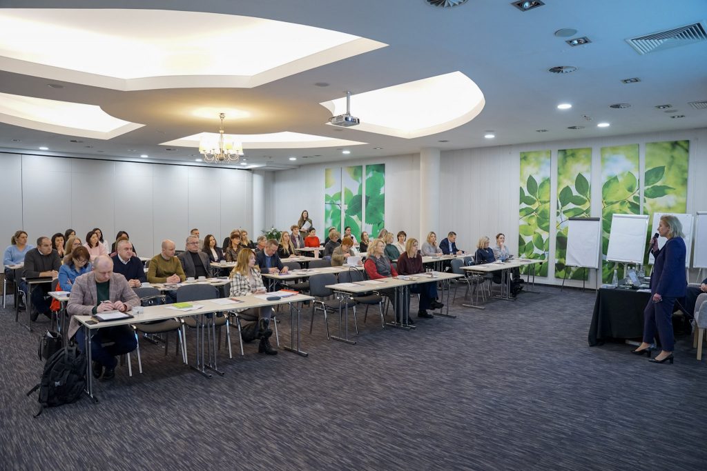 Sala konferencyjna z uczestnikami siedzącymi przy stołach, widok od przodu