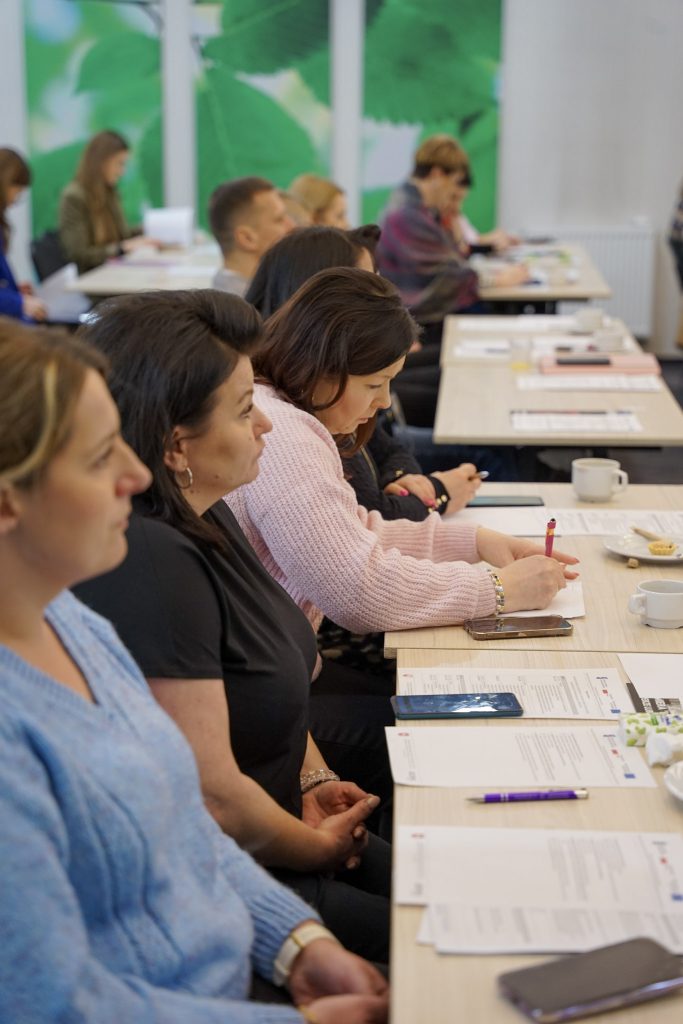 kobieta notuje w notatniku, pisze długopisem. obok siedzą inni ludzie i słuchają wykładu