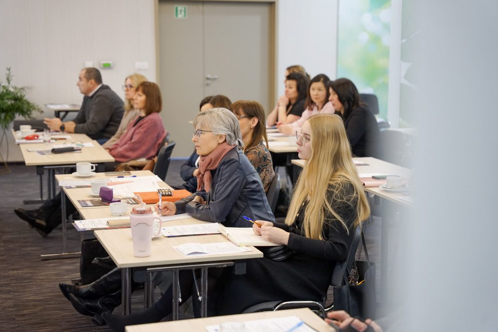 ludzie słuchający wykładu, siedzą przy stołach, patrzą przed siebie