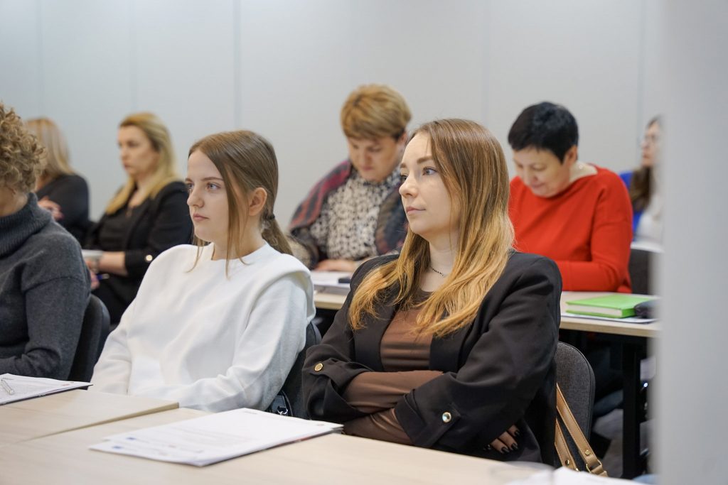 dwie kobiety słuchają wykładu, za nimi dwie kobiety notują